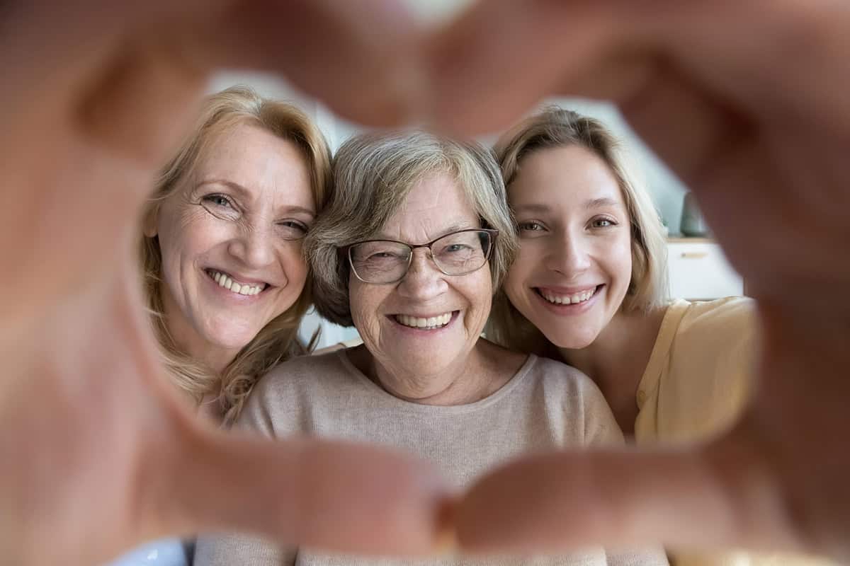Joyful Happy Loving Grandma, Mature Mother And Young Adult Granddaughter Woman Looking, Smiling At Camera Through Hand Heart Frame. Cute Portrait Of Loving Three Family Female Generations Having Fun